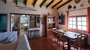 A cozy living room with a wooden dining table, a sofa, and a kitchen area visible through an open doorway.