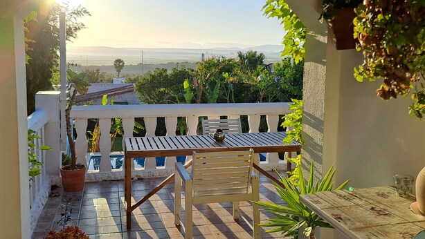 A balcony with a table and chairs, potted plants, and a view of the landscape.