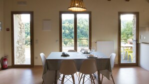 Een eetruimte met een tafel gedekt voor vier personen, houten balken in het plafond en uitzicht op groen buiten de deur.