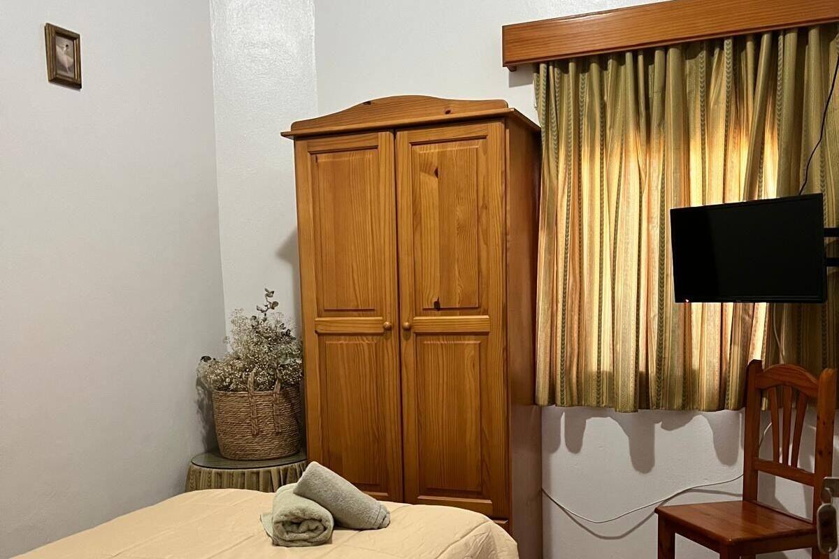 Une chambre à coucher avec un lit, une armoire en bois, une télévision, une chaise et une petite table.