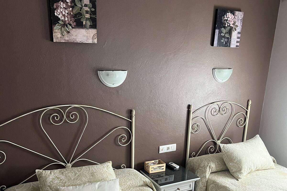 Une chambre d’hôtel avec deux lits, chacun doté d’une tête de lit, d’une table de chevet et d’une petite table de nuit. Il y a des serviettes sur les lits et une télécommande sur la table de nuit.