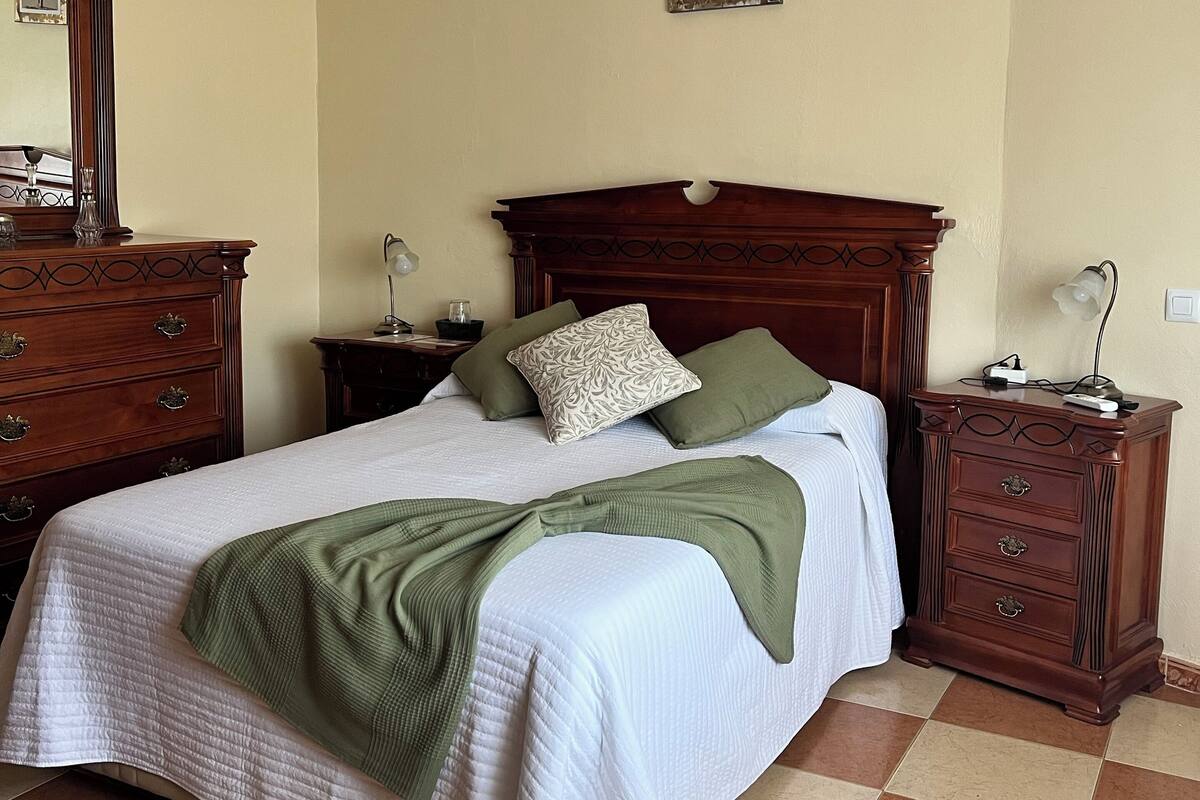 Un lit bien fait, avec une couverture verte, une tête de lit en bois et deux tables de chevet dotées de lampes.