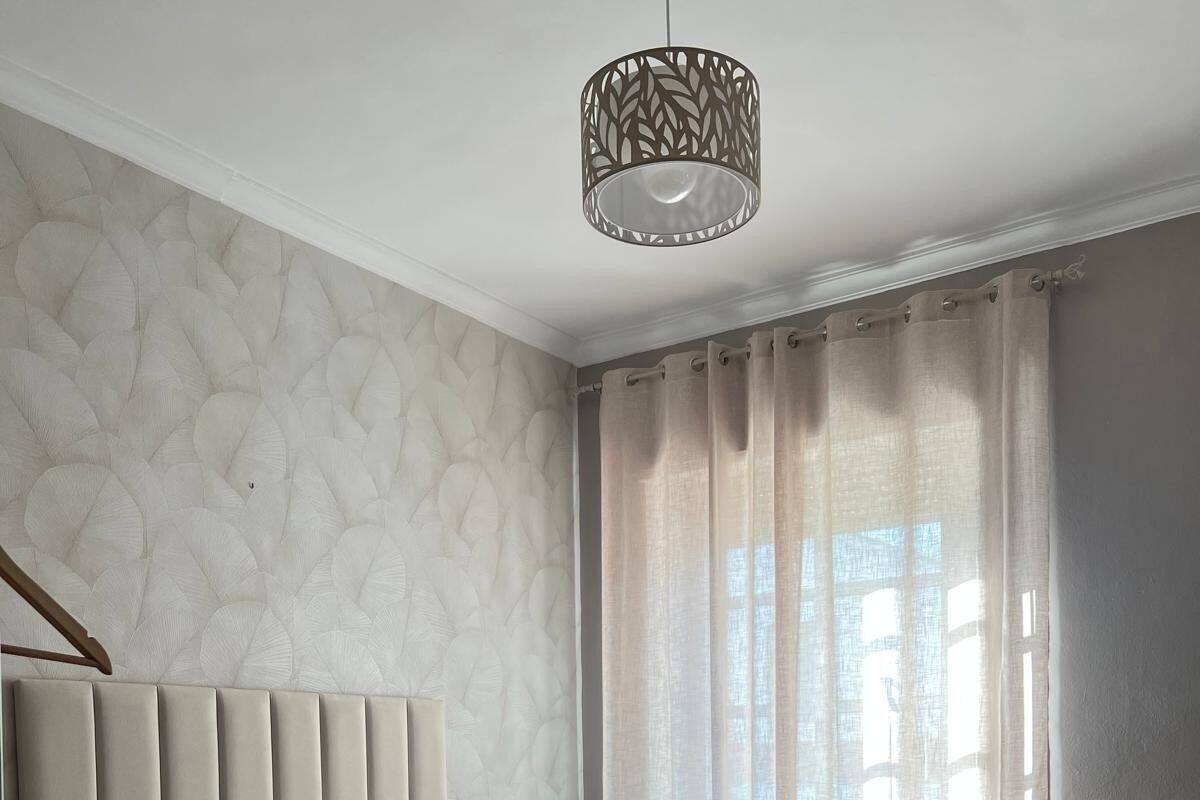 Une chambre avec deux lits, un mur décoré de motifs, un luminaire suspendu et une fenêtre avec des rideaux.