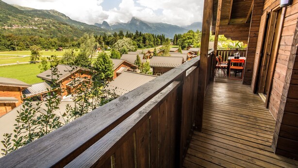 Ein Holzbalkon mit Blick auf eine gebirgige Landschaft und mehrere Holzhäuser.