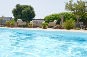 Uma área de piscina com espreguiçadeiras e plantas em vasos.