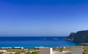 Vista costeira com edifícios, céu azul claro e o mar.