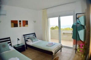 Quarto com duas camas, varanda com vista e parede com arte abstrata.