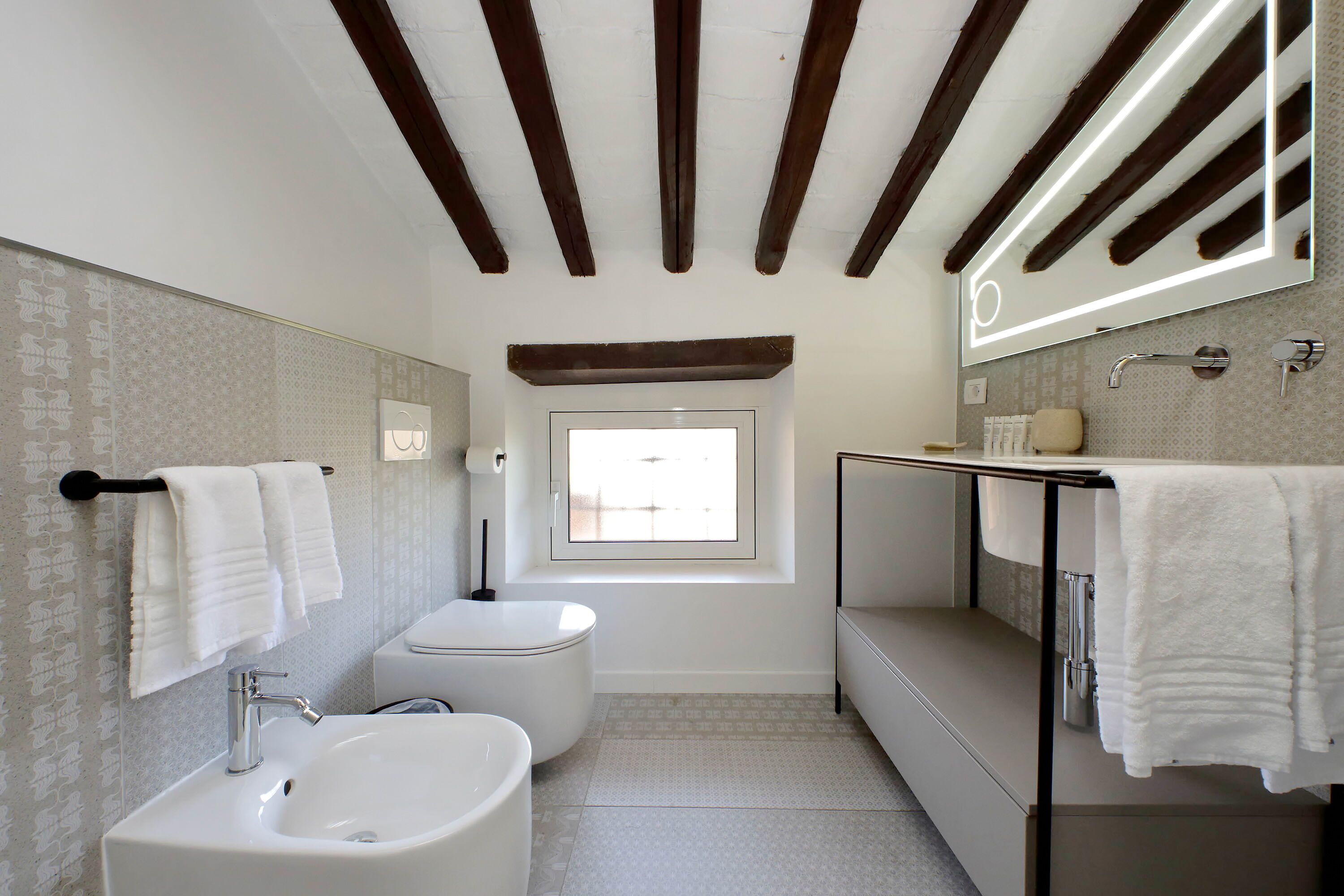 Un baño moderno con bañera, lavamanos e inodoro. Hay una ventana que proporciona luz natural y un espejo sobre el lavamanos.