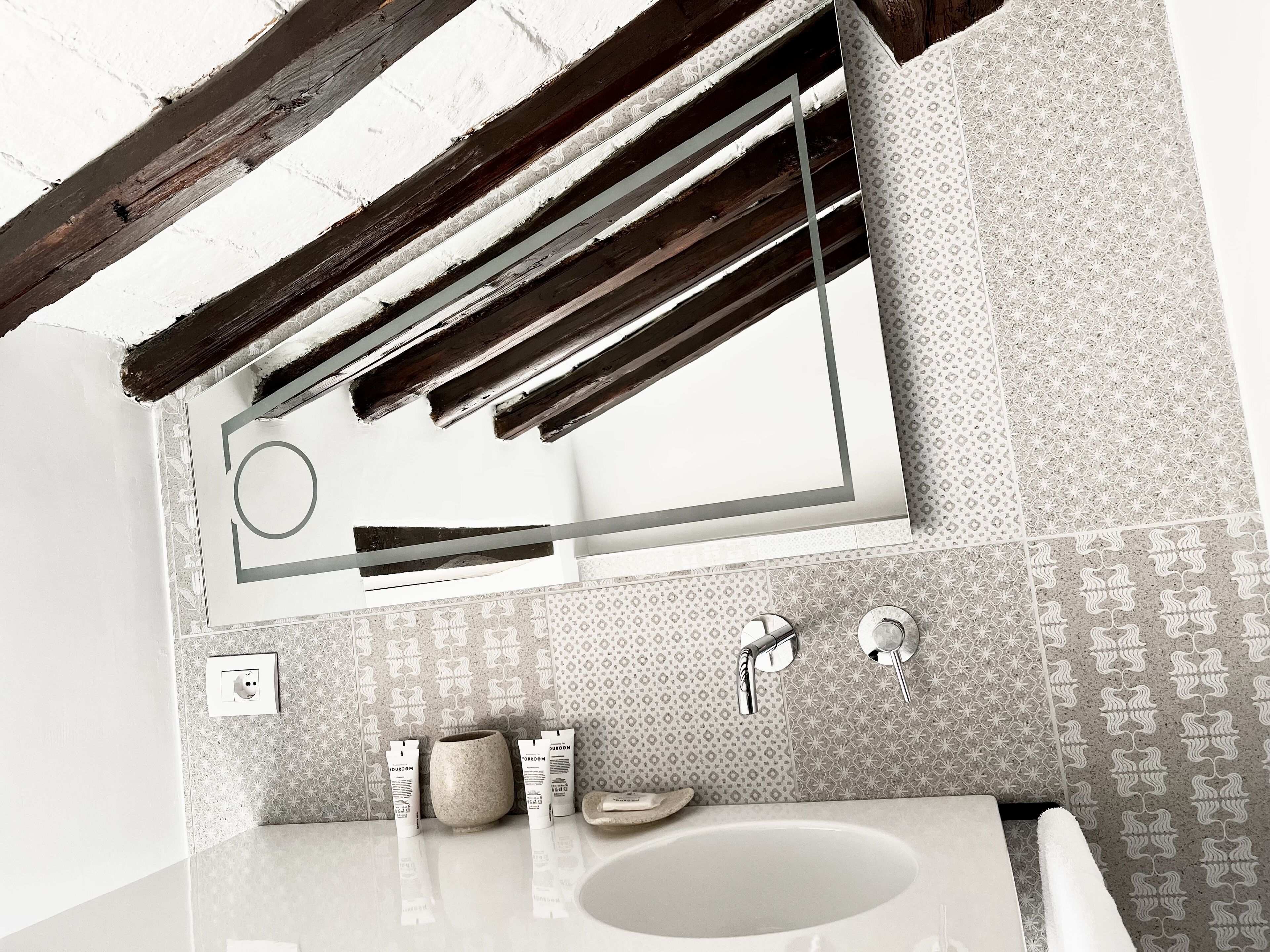 A bathroom with a large mirror, two sinks, a toilet, and patterned tiles.