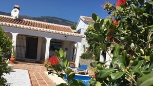 Een villa met een betegeld terras, een zwembad en weelderige begroeiing.