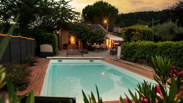 A rectangular swimming pool with a wooden deck, surrounded by greenery and a house with outdoor lighting. - Charming cottage with large pool, garden & views of Pyrénées, near Carcassonne (Montazels)