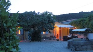 A building with a gravel driveway, a large tree in the foreground, and string lights around the entrance. - Charming cottage with large pool, garden & views of Pyrénées, near Carcassonne (Montazels)