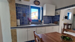 Una cucina con piastrelle blu e bianche, una finestra con vista, mobili bianchi e un tavolo da pranzo in legno con sedie.
