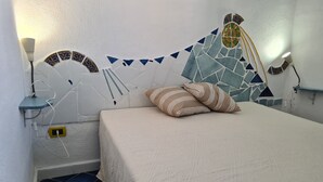 Una camera da letto con un letto, cuscini, un comodino, una lampada a parete e un mosaico decorativo al muro.