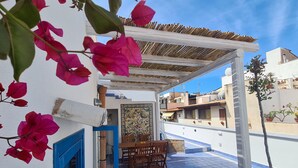 Una terrazza con tavolo e sedie, un vaso di fiori e vista sugli edifici circostanti.