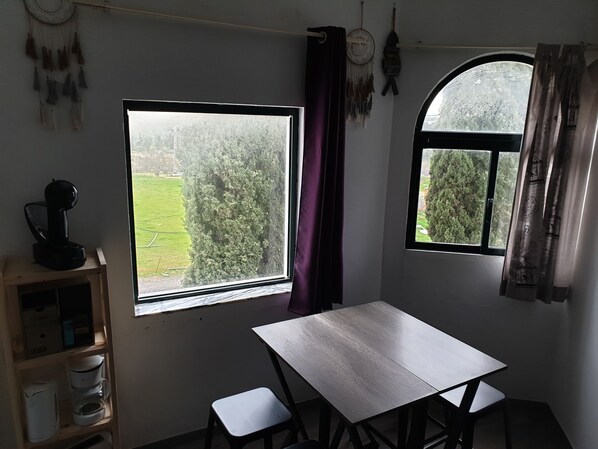 A room with a table and chairs, a window with a view of trees, and a shelf with kitchen items. - Apartment in the Algarve, Alvor (Alvor)