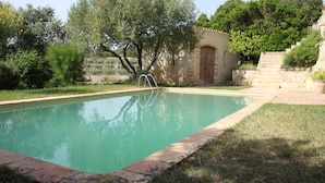 Une piscine bordée d’un mur en pierre et dotée d’une porte en bois, le tout entouré de verdure et d’arbres.