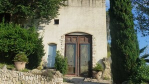 Un bâtiment en pierre avec une porte en bois, entouré de verdure et sous un ciel dégagé.