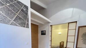 Un espacio habitable pequeño y de concepto abierto, con una mesa y sillas de madera para comer, una puerta corrediza que da a un dormitorio y una obra enmarcada en la pared.