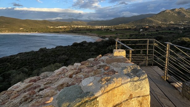 Un paisaje costero con un camino de madera que lleva a un promontorio rocoso con vista al mar.