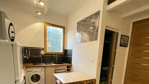 Cocina compacta con lavadora, una mesa con sillas y ventana con vista a árboles.