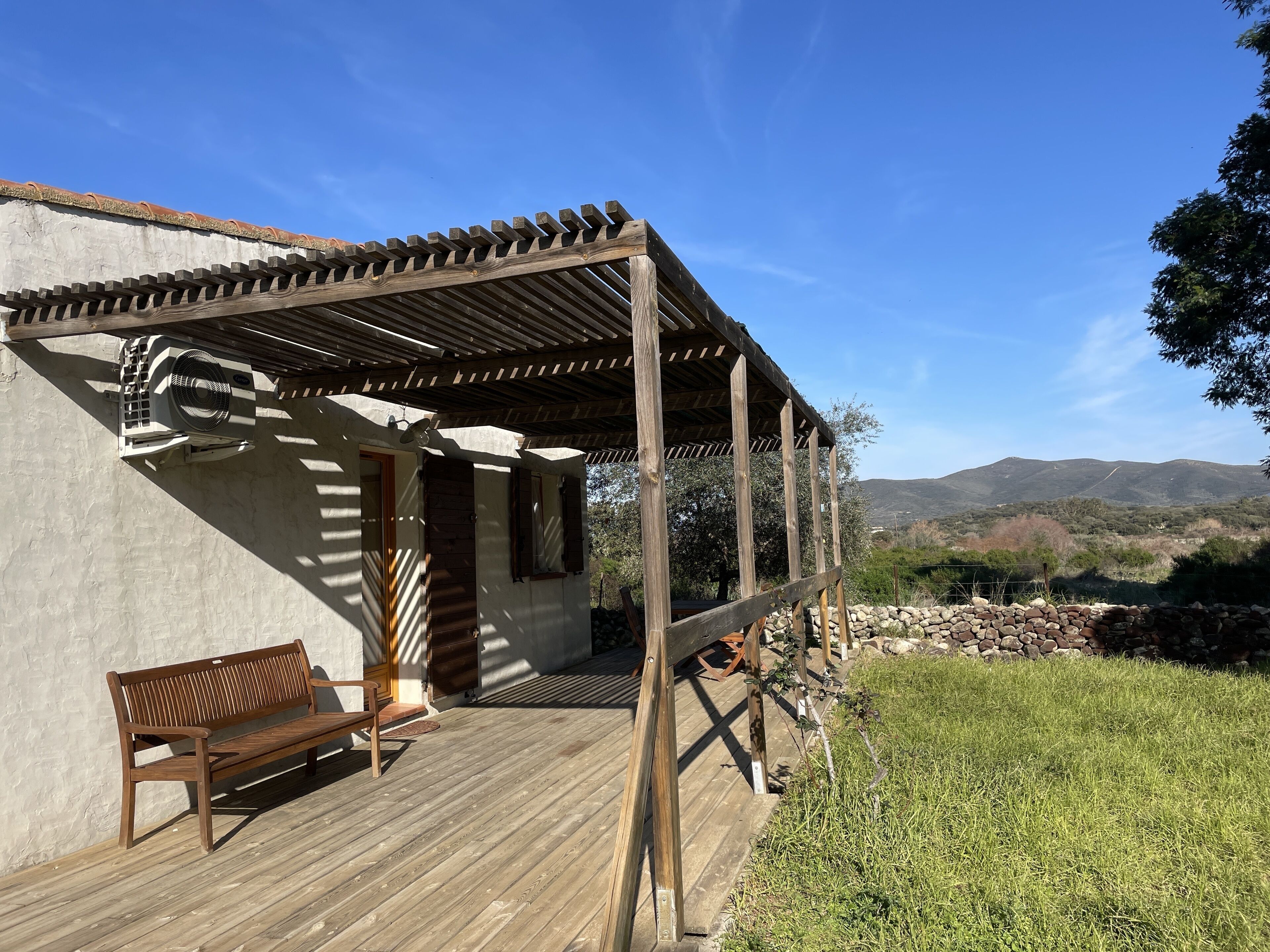 A wooden deck with a bench, a pergola, and a stone wall.