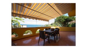 Eine Terrasse mit Tisch und Stühlen, Blick aufs Meer und eine Holz-Pergola.