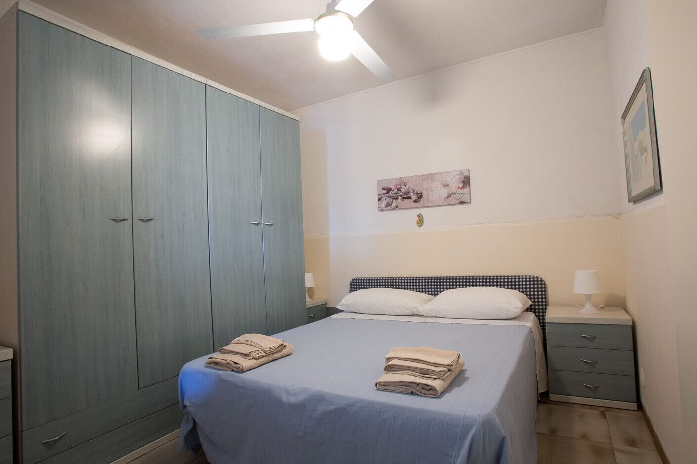 A bedroom with a bed, two bedside tables, a wardrobe, and a ceiling fan.