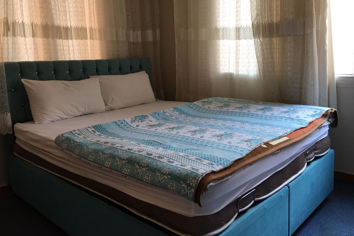 Un lit avec une couvre-lit à motifs, une tête de lit capitonnée et deux oreillers.