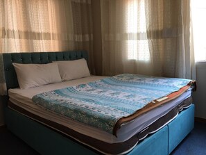 Ein Bett mit einem gemusterten Überwurf, einem gepolsterten Kopfteil und zwei Kissen.