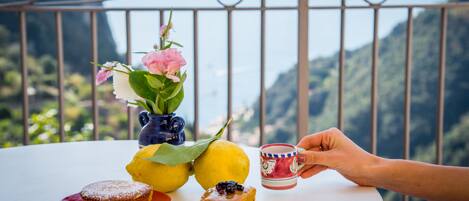 Una mesa con un postre, un florero con flores y una taza, frente a un paisaje montañoso.