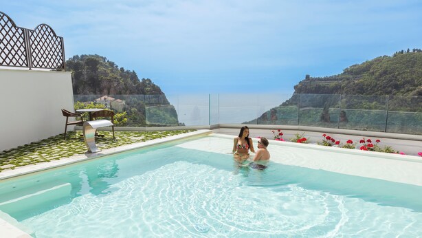 A pool with clear water, surrounded by a white wall and a view of cliffs. - Palazzo San Giovanni (Scala)