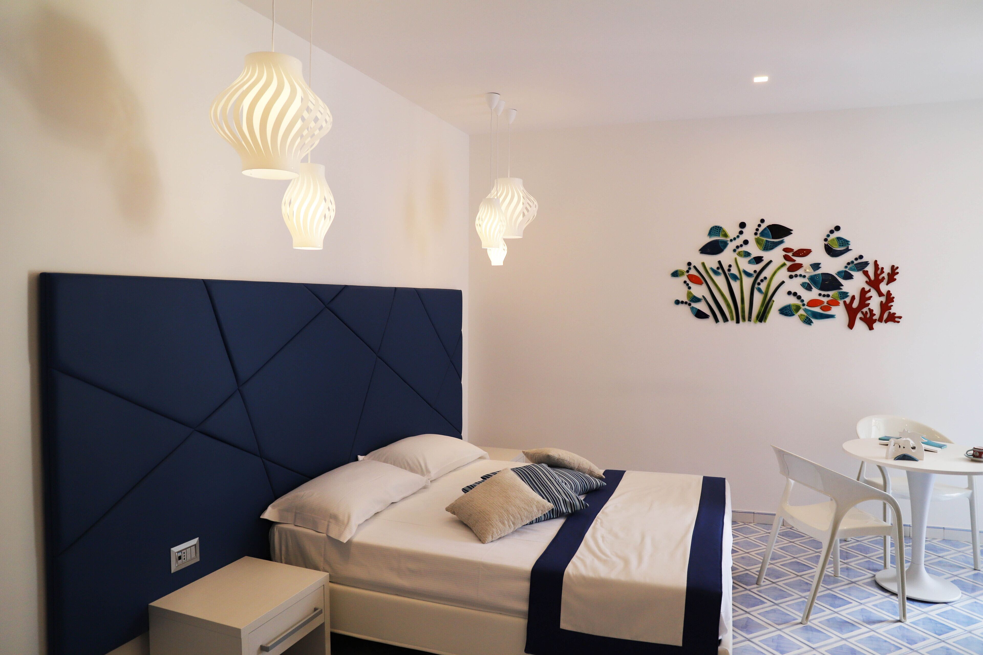 Un dormitorio ordenado con cama, mesita de noche y una pequeña mesa blanca con sillas.