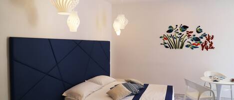 Un dormitorio ordenado con cama, mesita de noche y una pequeña mesa blanca con sillas.