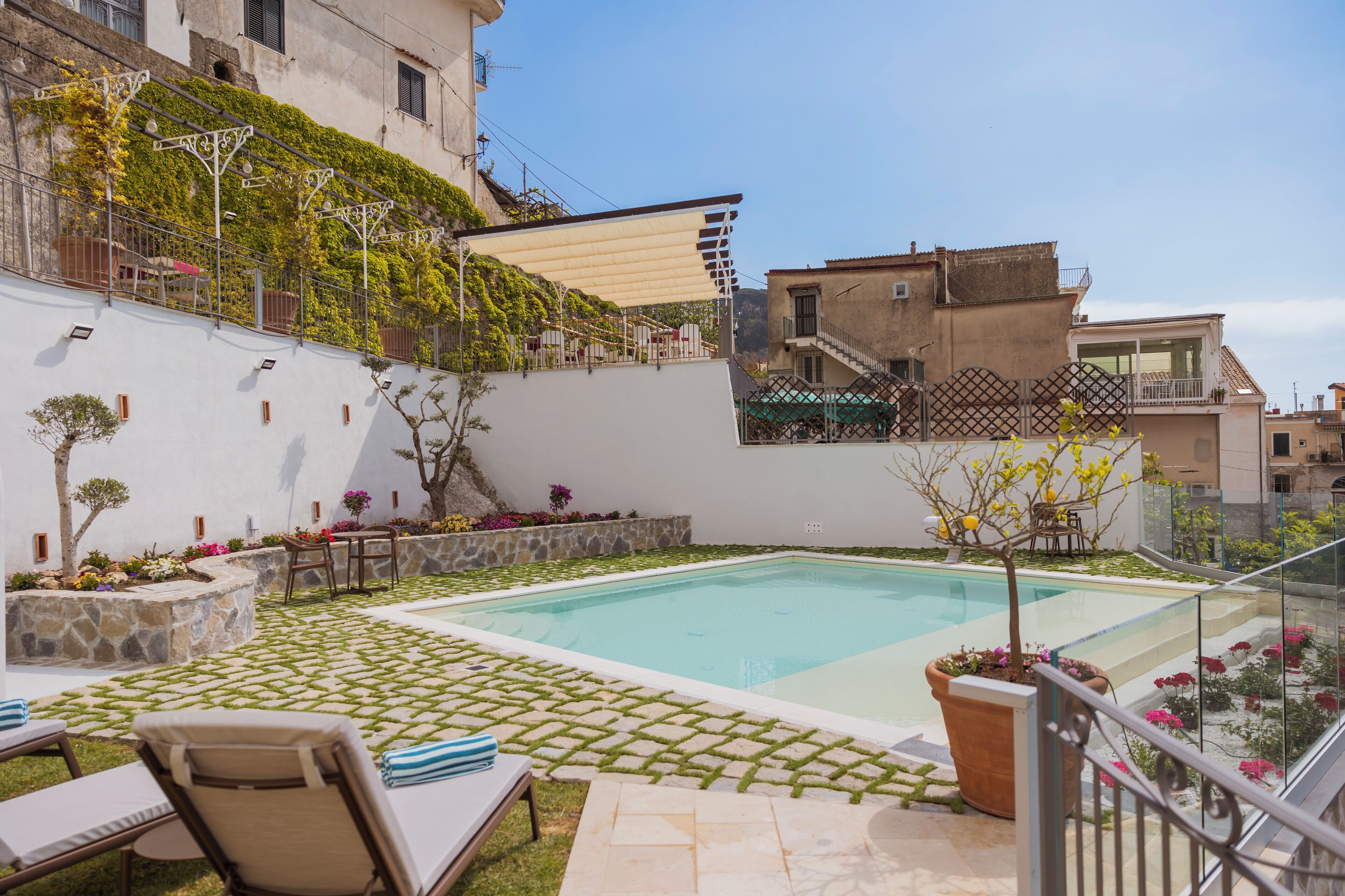 Una piscina con solárium azulejado, sillas de descanso y plantas en macetas.