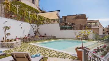 Una piscina con solárium azulejado, sillas de descanso y plantas en macetas.