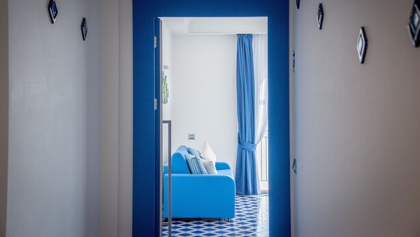 A hallway leading to a room with a blue sofa and a window with blue curtains. - Palazzo San Giovanni (Scala)