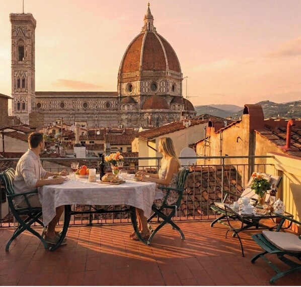 A terrace with a table set for two, overlooking a historic building with a dome and bell tower.