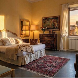 A bedroom with a bed, bedside lamps, a dresser, a painting, and a window with curtains.