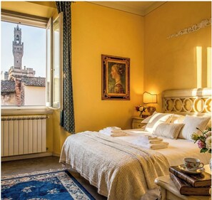 A hotel room with a bed, a window with curtains, a painting, a nightstand, and a lamp.