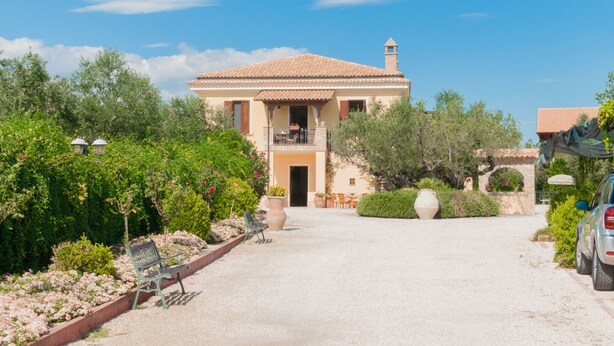 Eine Villa mit Ziegeldach, einem Balkon und einem Garten mit Bänken und Blumentöpfen.