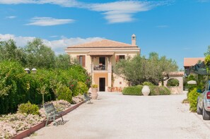 Eine Villa mit Ziegeldach, einem Balkon und einem Garten mit Bänken und Blumentöpfen.