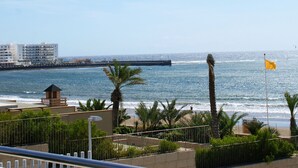 Une vue côtière avec une plage, des palmiers et un grand navire à l’horizon.