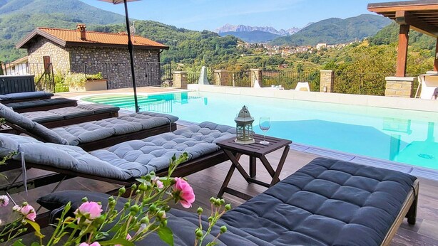 Zona junto a la piscina con sillones de descanso, una sombrilla y vistas a las montañas.