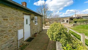 A stone house with a white door, a small porch, and a pathway leading to a green bush. - The Brambles - one bedroom Country Cottage near Dorset Coast. (Weymouth)