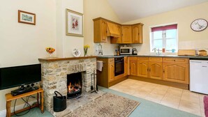 A cozy kitchen with wooden cabinets, a stone fireplace, a television, and a microwave. - The Brambles - one bedroom Country Cottage near Dorset Coast. (Weymouth)