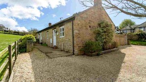 A stone cottage with a gravel driveway, a wooden fence, and a garden. - The Brambles - one bedroom Country Cottage near Dorset Coast. (Weymouth)