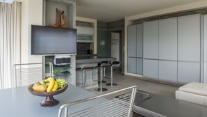 A modern kitchen with a flat-screen TV, a fruit bowl on the counter, and a dining area with a bar stool.