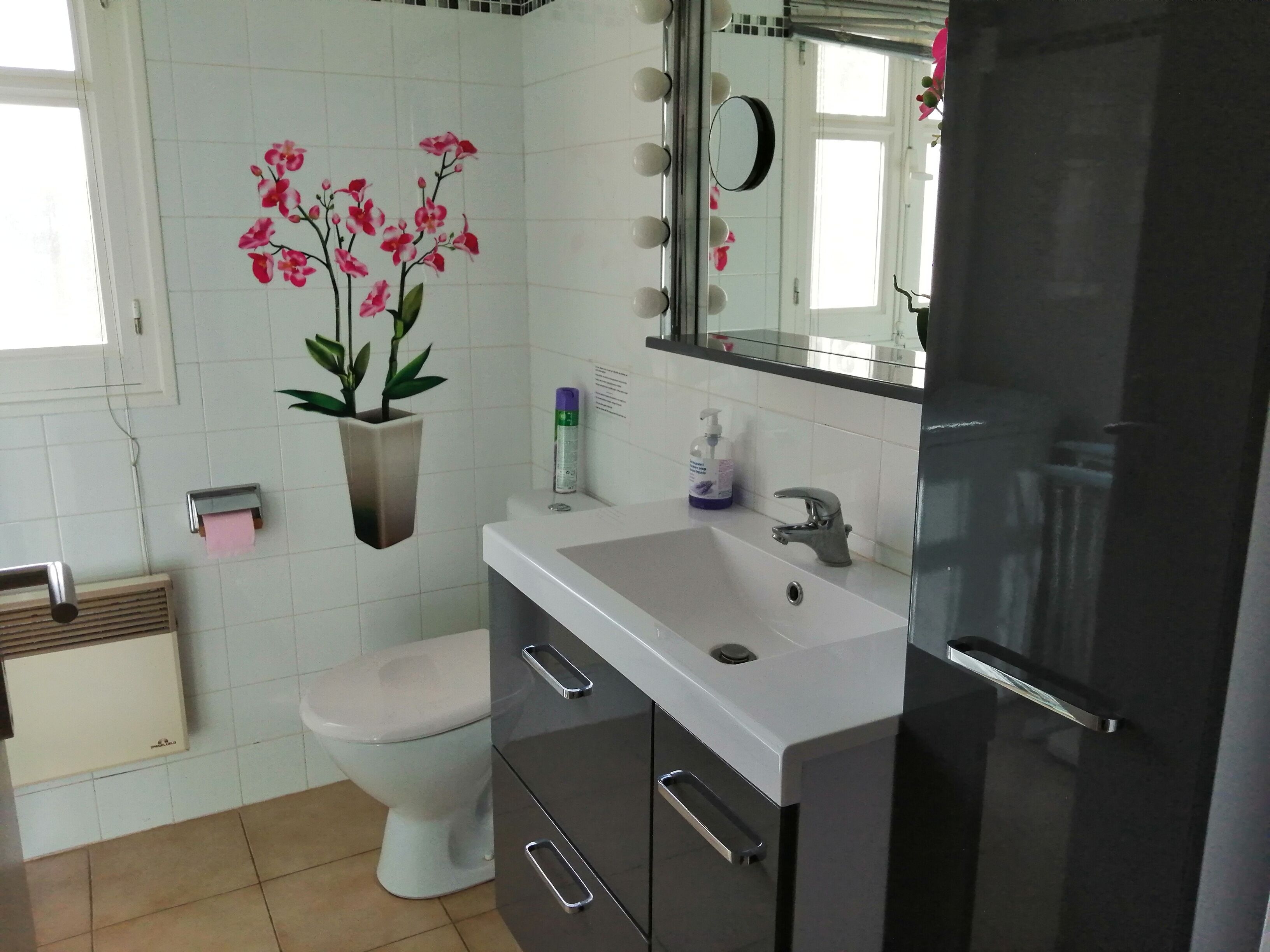 Ein Badezimmer mit Toilette, Waschbecken, Spiegel und einer Orchidee im Topf.