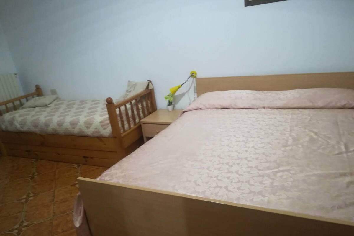 A bedroom with two wooden beds, a small bedside table with a vase of flowers, and a radiator on the wall.